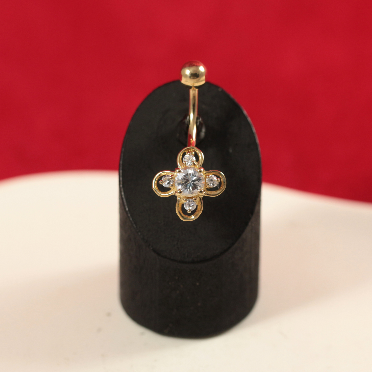 Close-up of 14K Gold Studded Clover Belly Ring displayed on a black stand, highlighting its intricate gold loops and gemstone-studded clover shape.