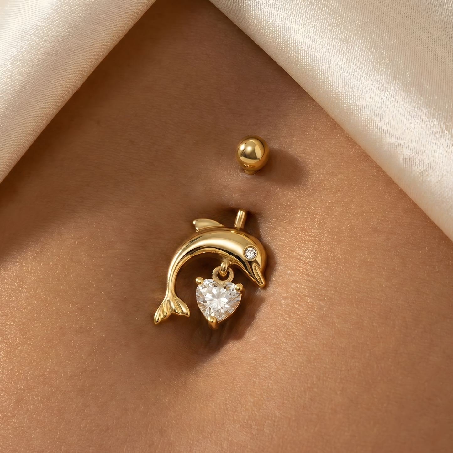14K gold dangling dolphin belly ring with heart-shaped cubic zirconia, worn on navel for a chic and elegant body jewelry statement.