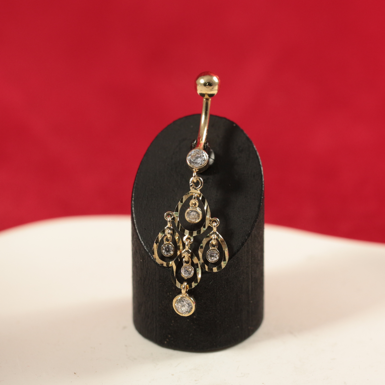 Close-up of 14K Gold CZ Tear Shape Belly Ring displayed on a black stand, highlighting its intricate dangling design and polished gold finish.
