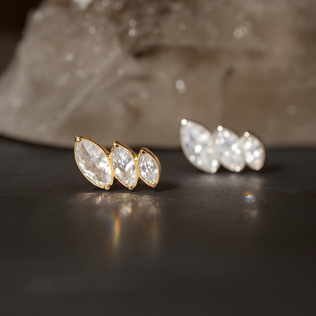 Gold and silver G23 Titanium Triple Marquise CZ Flat Back Studs displayed on a dark surface, perfect for tragus and labret piercings.